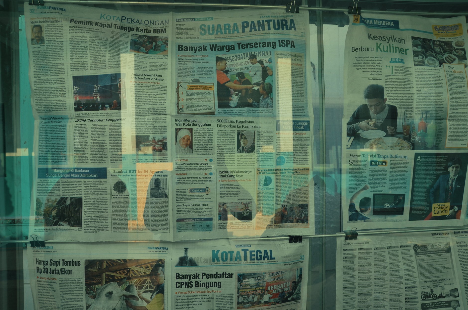 Radio and newspaper newsroom monitors showing local civic news alongside a public broadcasting studio microphone