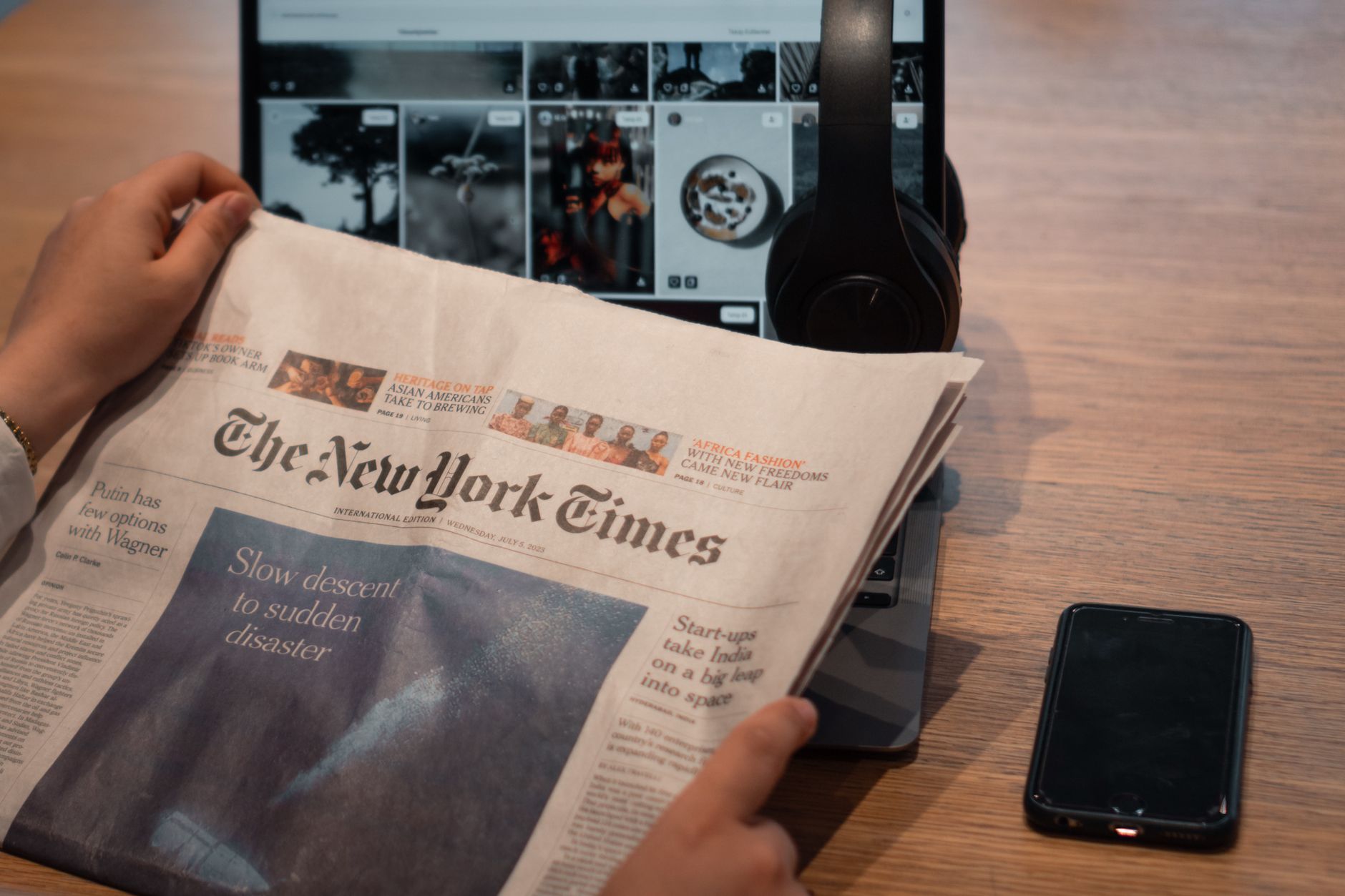 A folded newspaper opinion section resting on a wooden desk beside reading glasses