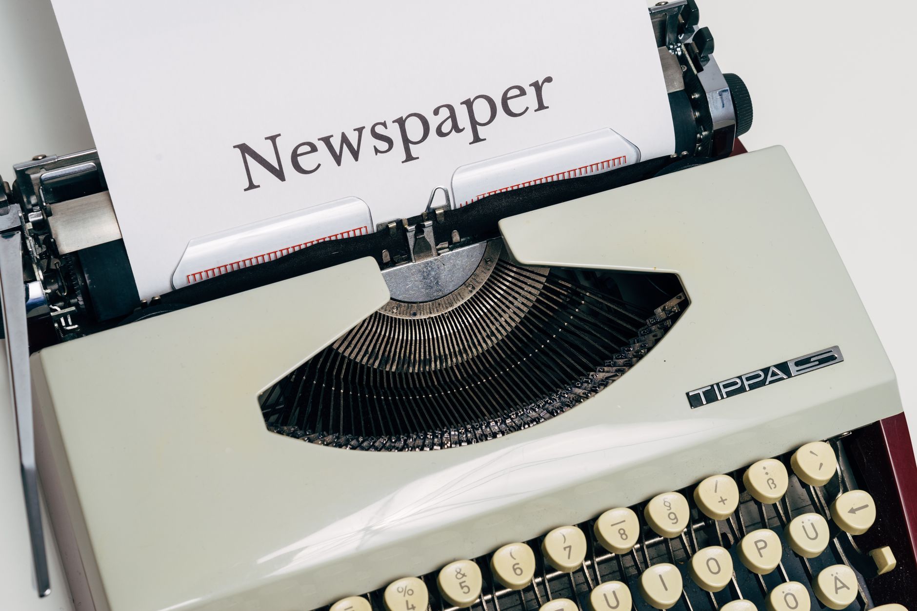 Newsroom desk with printed opinion page proofs beside a laptop showing a wire service feed