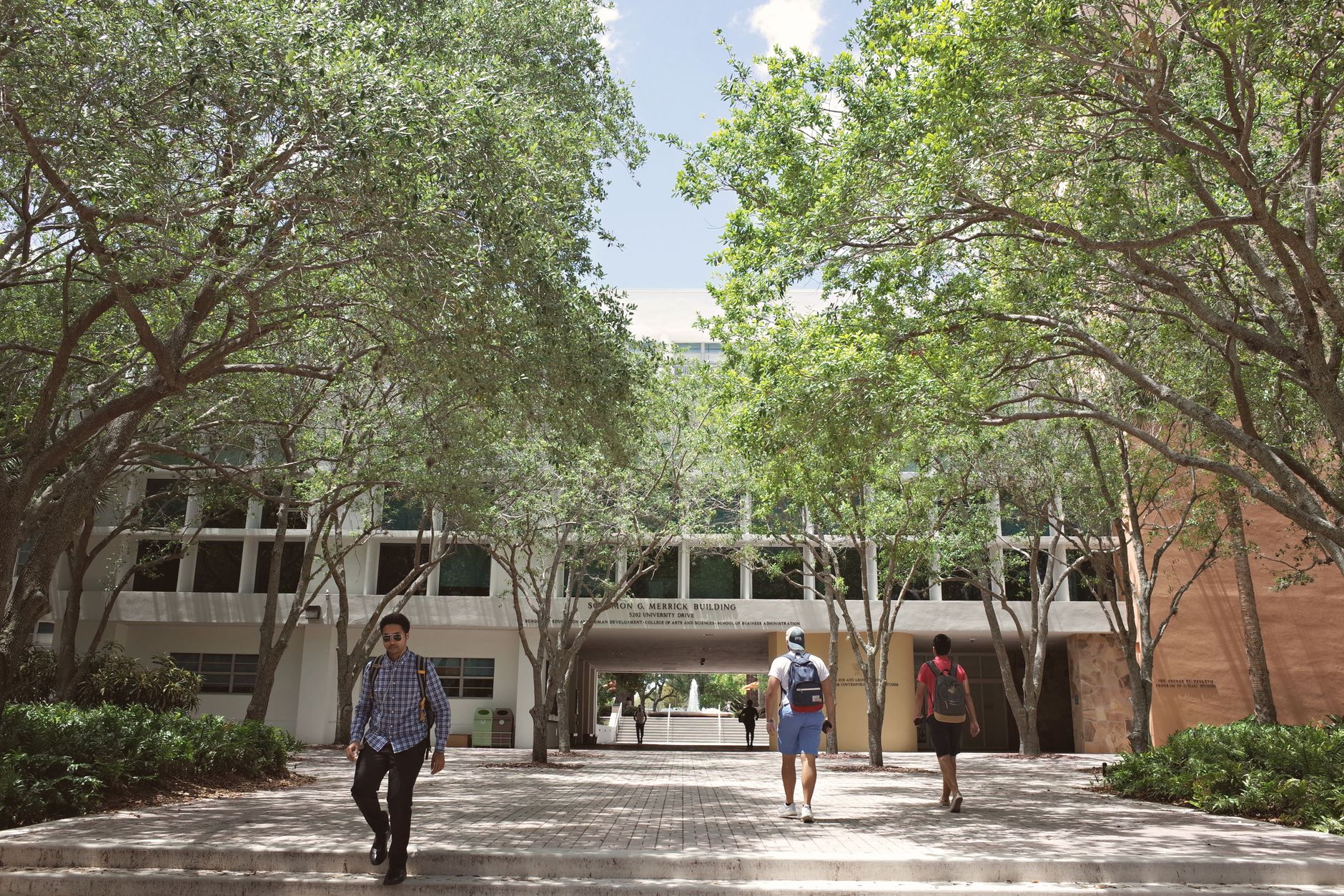 A university quad with students walking past a bulletin board covered in flyers under autumn trees.